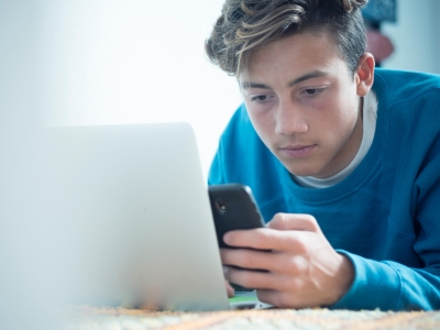 young male looking at smart phone next to an open laptop