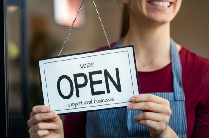 a woman flips a business sign to 'Open'