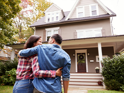 A man and woman embrace in front of a two-story home