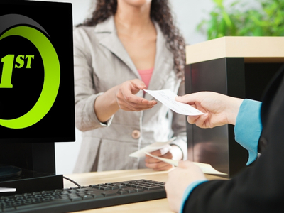 A person behind a desk hands another person a piece of paper