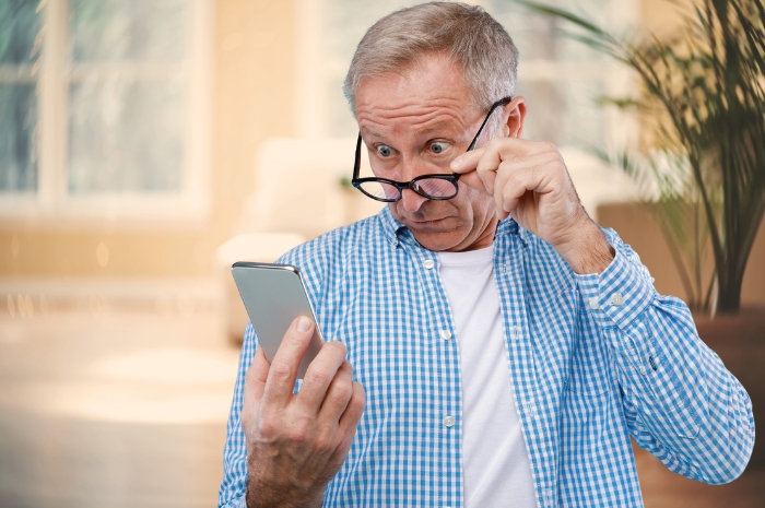 a mature man looks over his glasses while reviewing his mobile phone screen